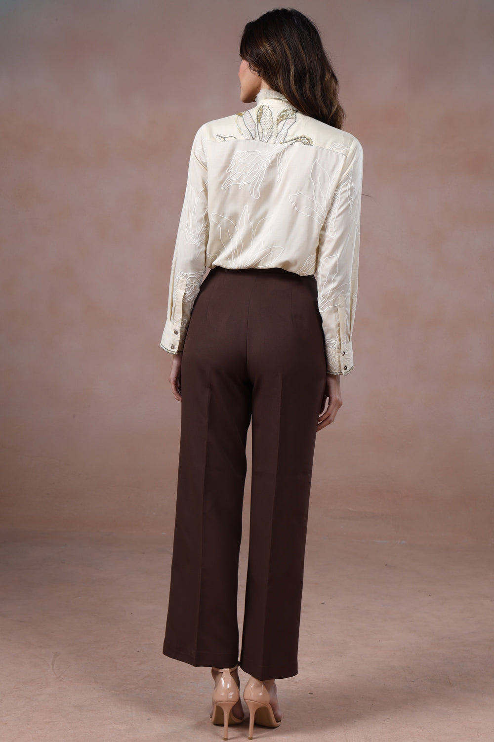 Woman wearing a white blouse and brown pants against a beige background