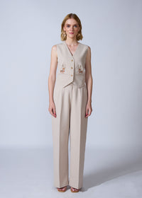 Woman wearing a beige vest and pants set with embroidery on a white background