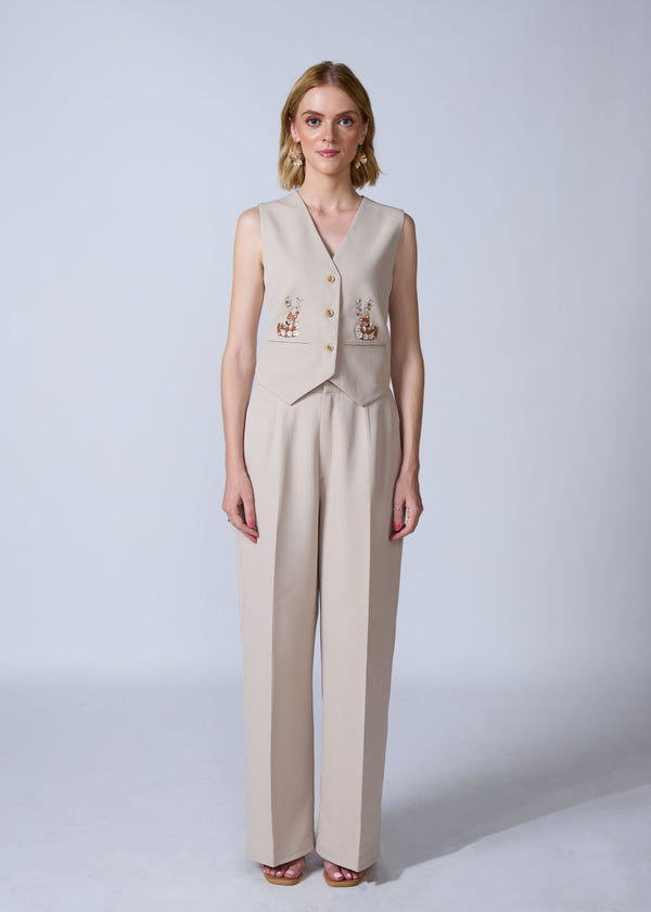 Woman wearing a beige vest and pants set with embroidery on a white background