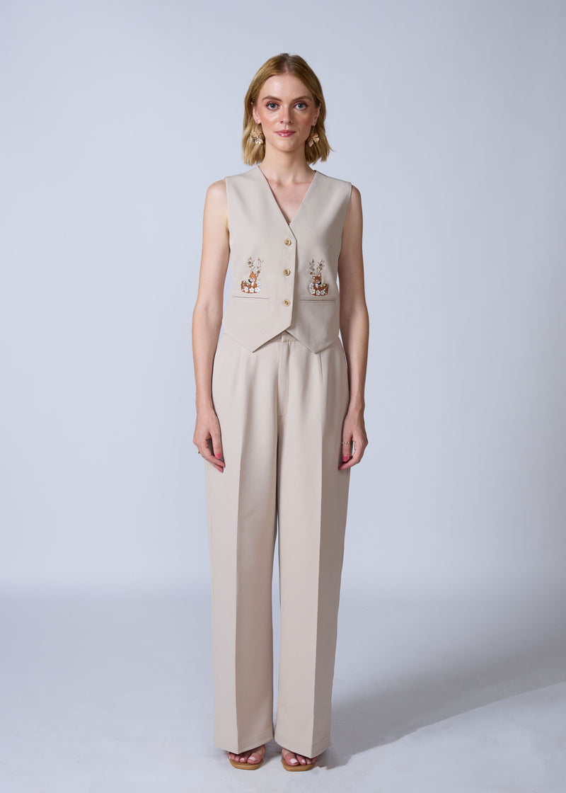 Woman wearing a beige vest and pants set with embroidery on a white background