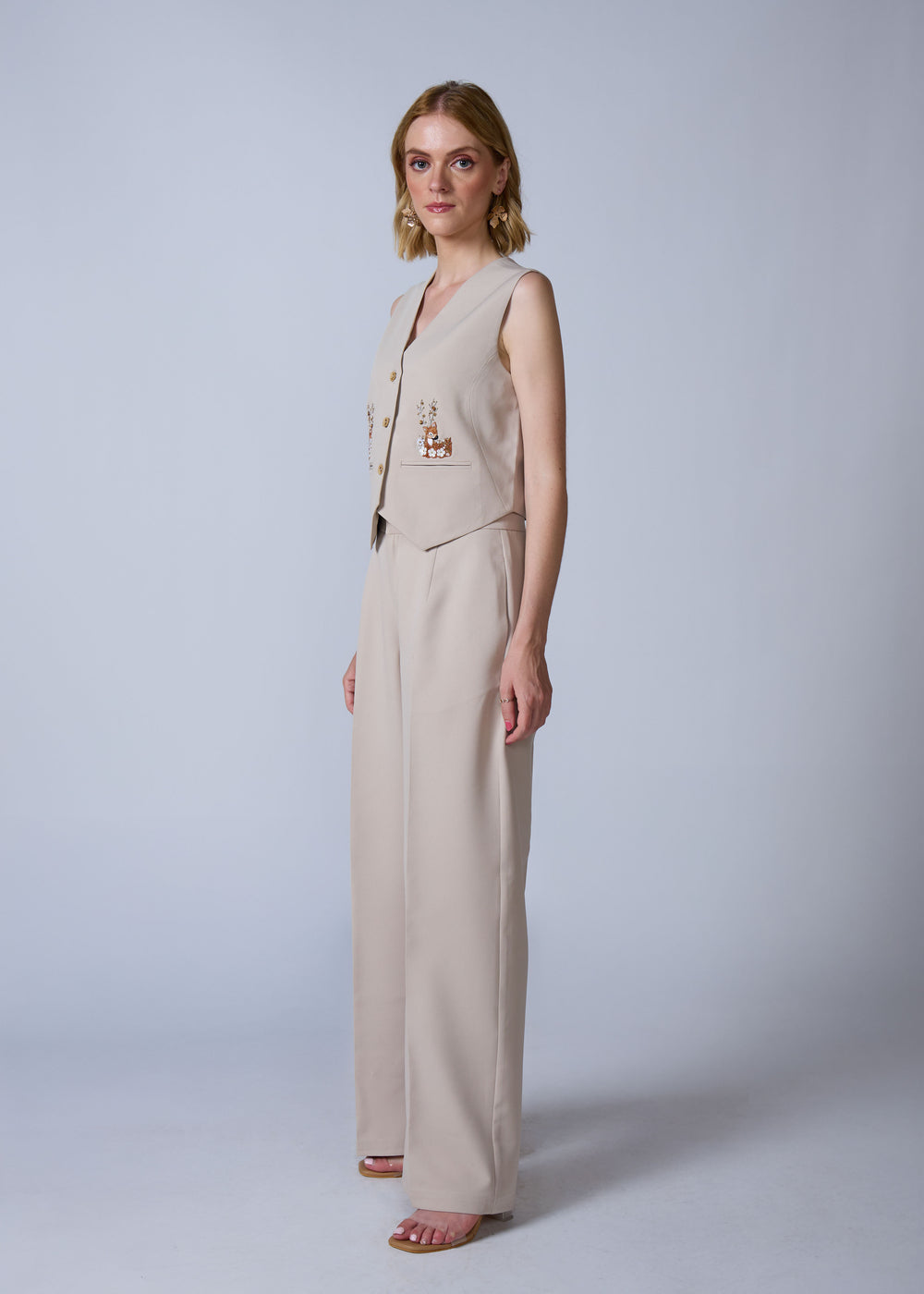 Woman wearing a beige sleeveless top and wide-leg pants on a white background