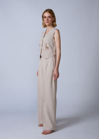 Woman wearing a beige sleeveless top and wide-leg pants on a white background
