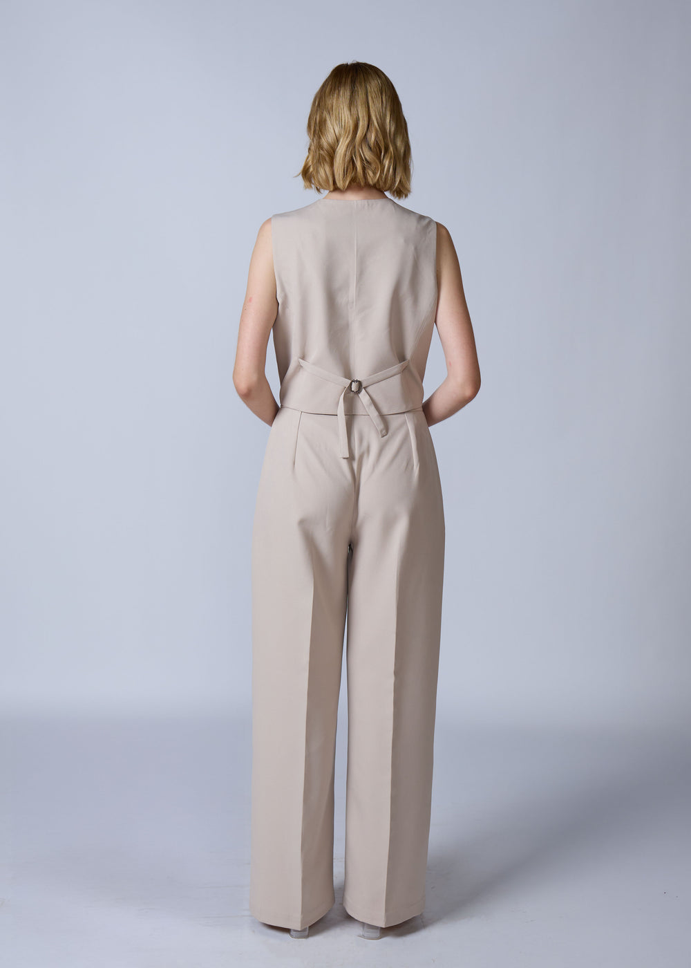 Woman wearing a beige sleeveless jumpsuit on a plain background