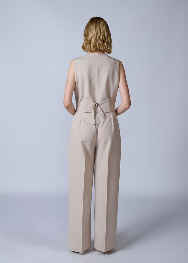 Woman wearing a beige sleeveless jumpsuit on a plain background