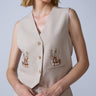 Woman wearing a beige vest with floral embroidery on a plain background