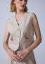 Woman wearing a beige vest with floral embroidery on a plain background