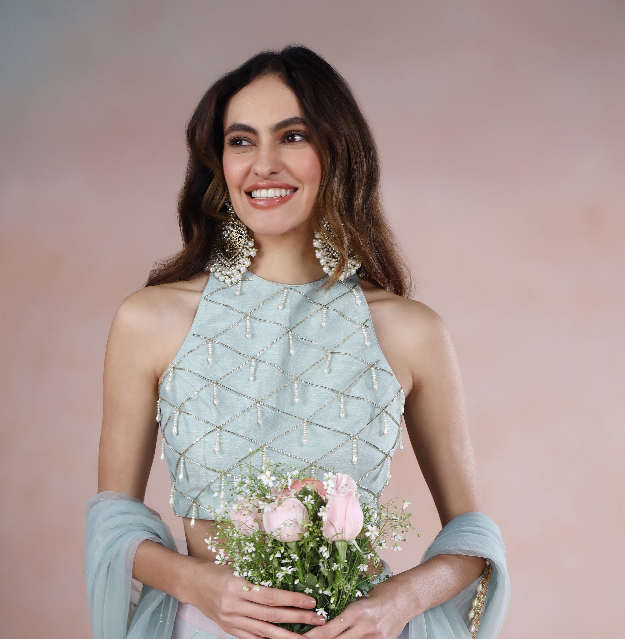 Woman in a light blue and pink traditional outfit holding flowers against a pink background