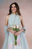 Woman in a light blue and pink traditional outfit holding flowers against a pink background