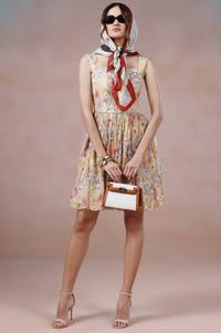 Woman in a floral dress with a red scarf, sunglasses, and a handbag against a plain background