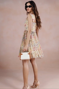 Woman in a floral dress holding a white clutch against a beige background