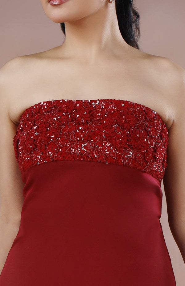 Woman wearing a strapless red dress with beaded details on a beige background