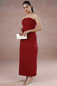 Woman in a strapless red dress holding a clutch against a plain background