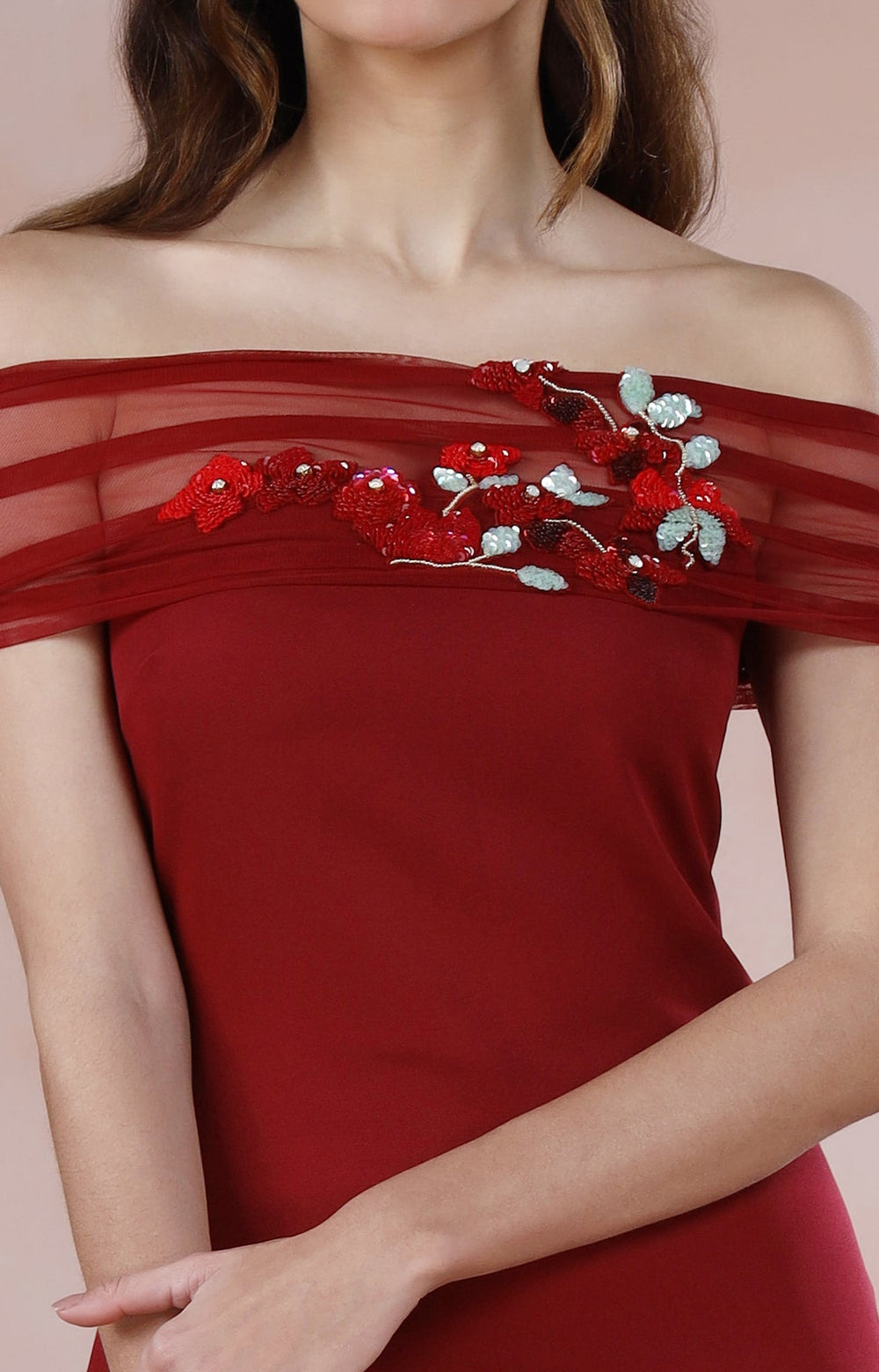 Woman wearing a red off-shoulder dress with floral embroidery on a pink background