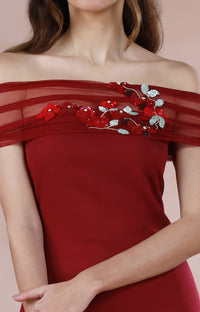 Woman wearing a red off-shoulder dress with floral embroidery on a pink background