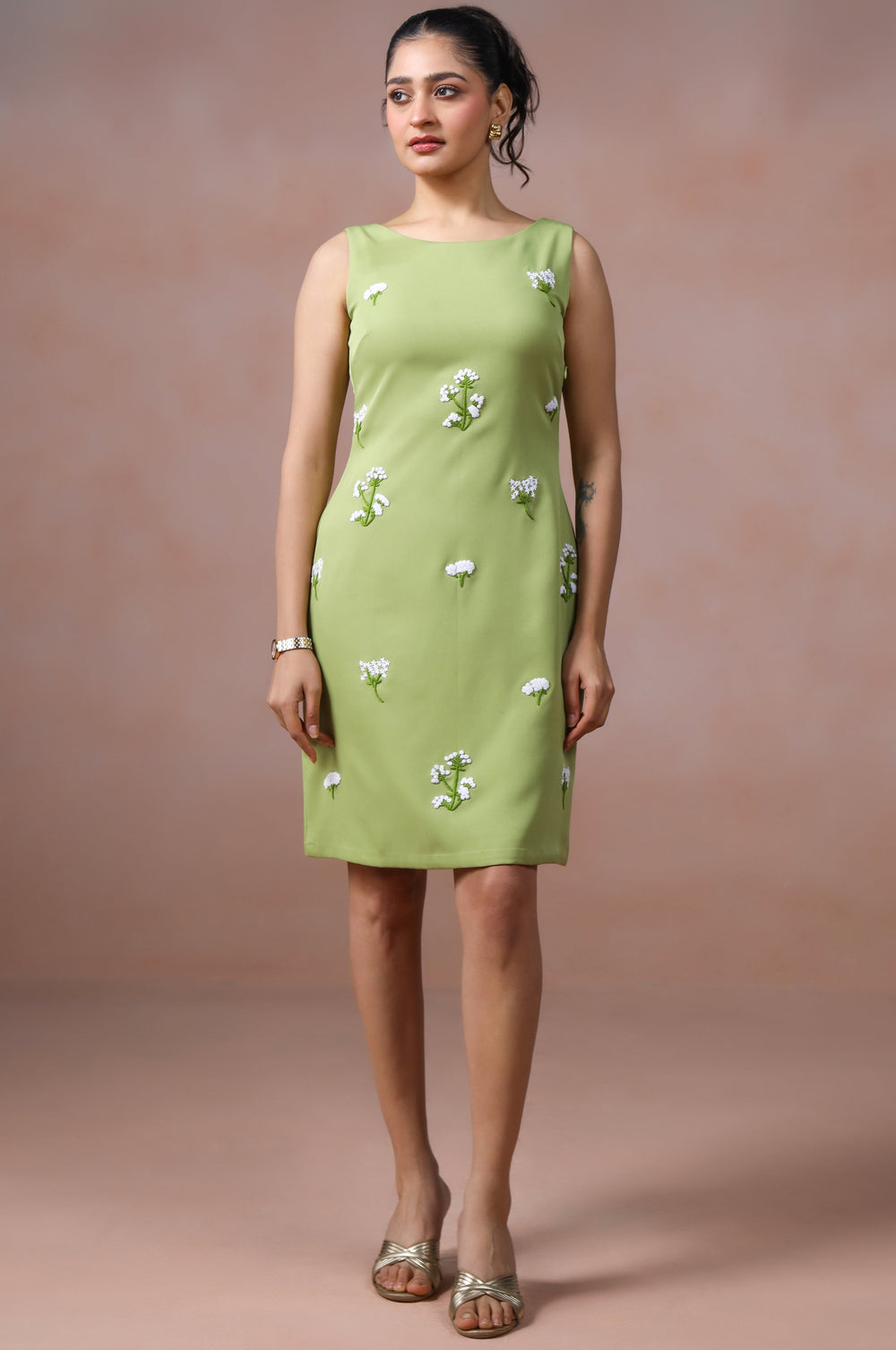 Woman wearing a light green dress with floral patterns against a plain background