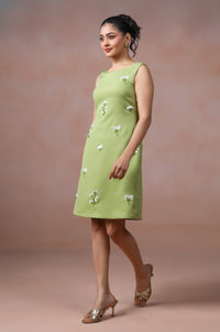 Woman wearing a green dress with floral embellishments against a brown background