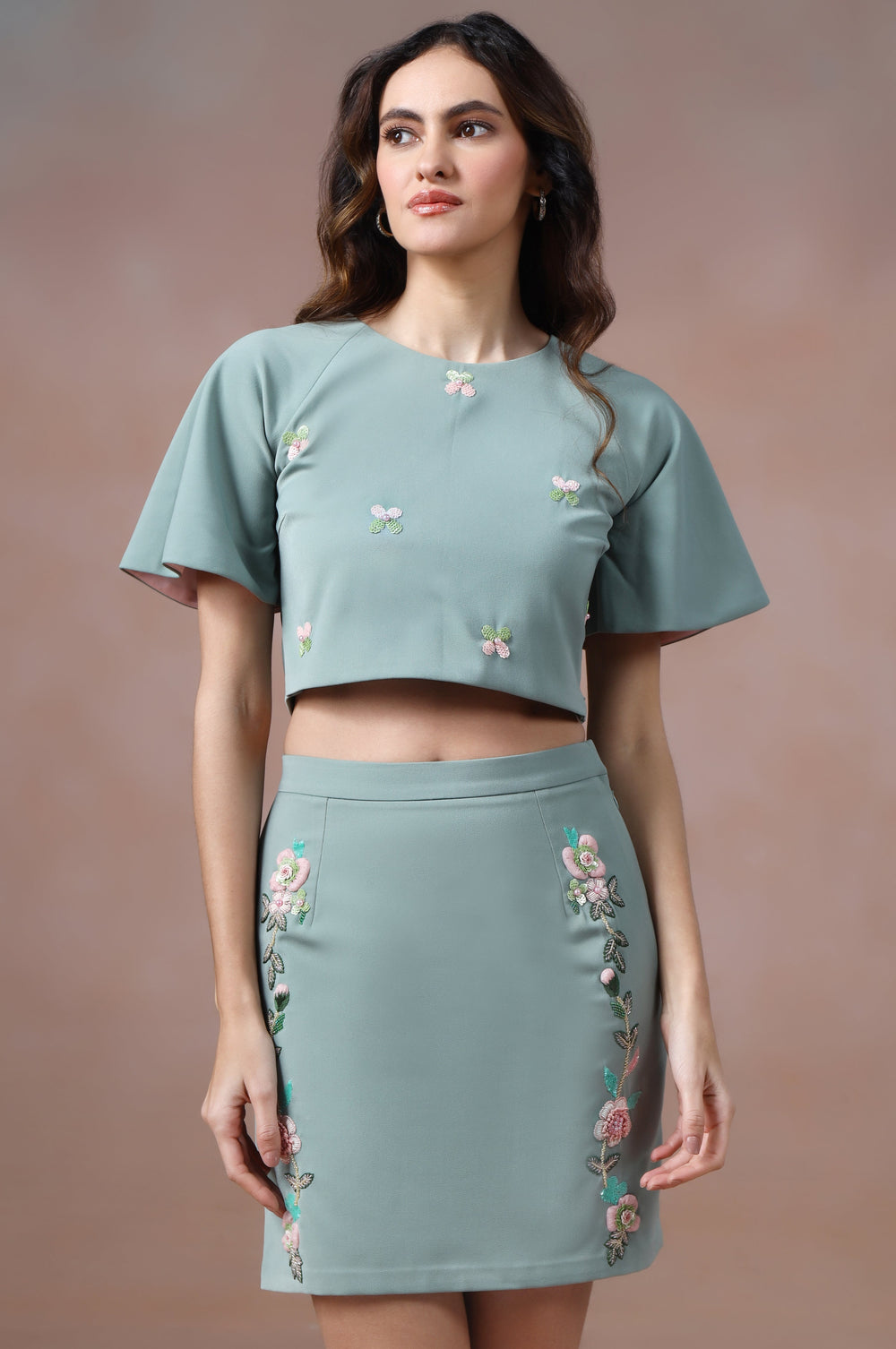 Woman wearing a matching green top and skirt with floral embroidery on a brown background