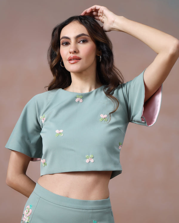 Woman wearing a matching green outfit with floral embroidery against a brown background