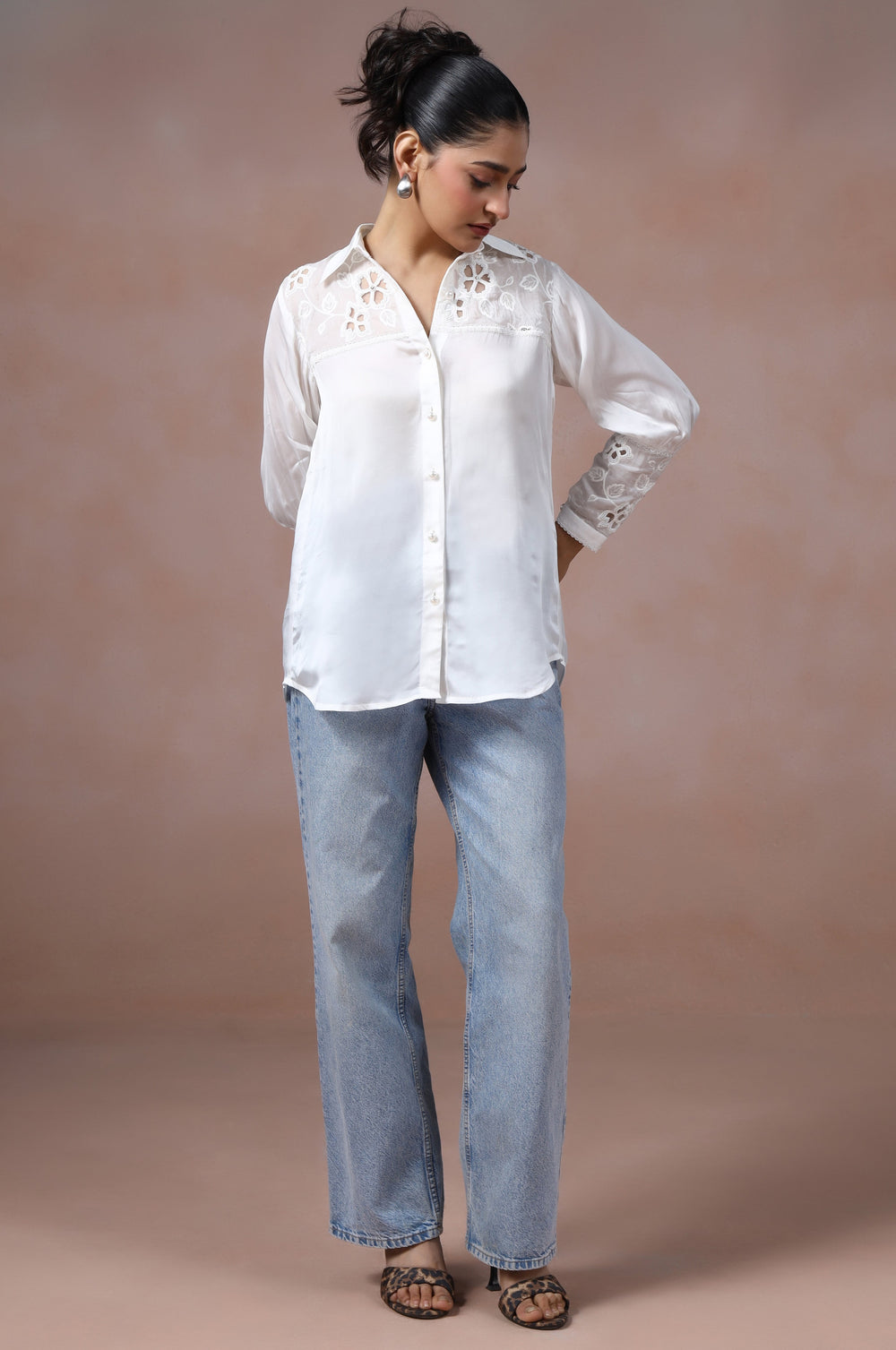 Woman wearing a white blouse and light blue jeans against a beige background