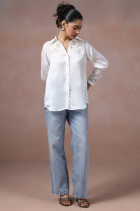 Woman wearing a white blouse and light blue jeans against a beige background