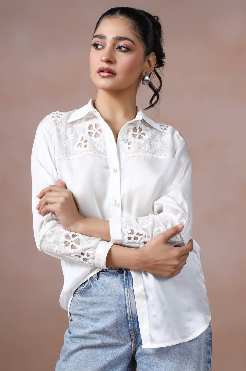 Woman wearing a white blouse with lace details and blue jeans against a brown background