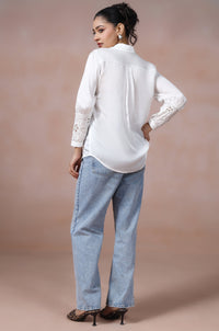 Woman wearing a white blouse and light blue jeans against a beige background