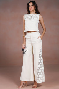 Woman wearing a white outfit with floral details against a brown background