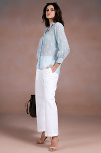 Woman wearing a light blue blouse and white pants against a beige background