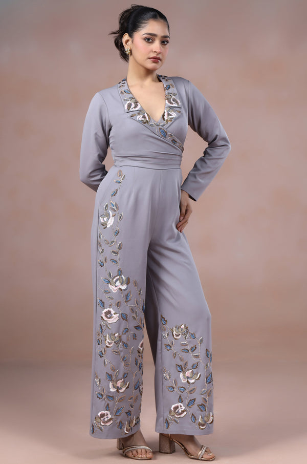 Woman wearing a gray jumpsuit with floral embroidery against a plain background