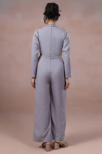 Woman wearing a light gray jumpsuit standing against a gradient background