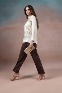 Woman in a white blouse and brown pants holding a clutch against a gradient background