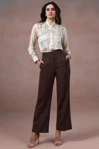 Woman wearing a white blouse and brown pants against a plain background