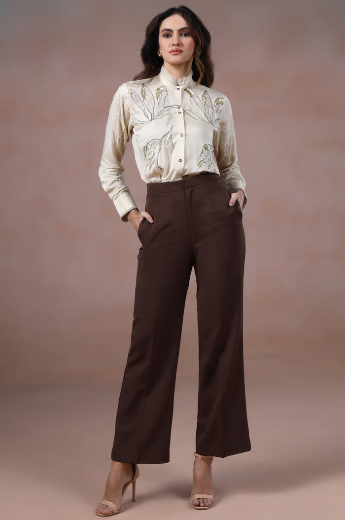 Woman wearing a white blouse and brown pants against a plain background