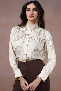 Woman wearing a cream floral blouse and brown pants against a brown background