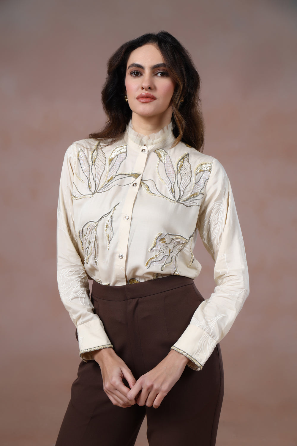 Woman wearing a cream floral blouse and brown pants against a brown background