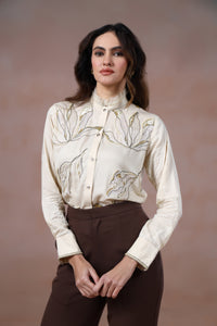 Woman wearing a cream floral blouse and brown pants against a brown background