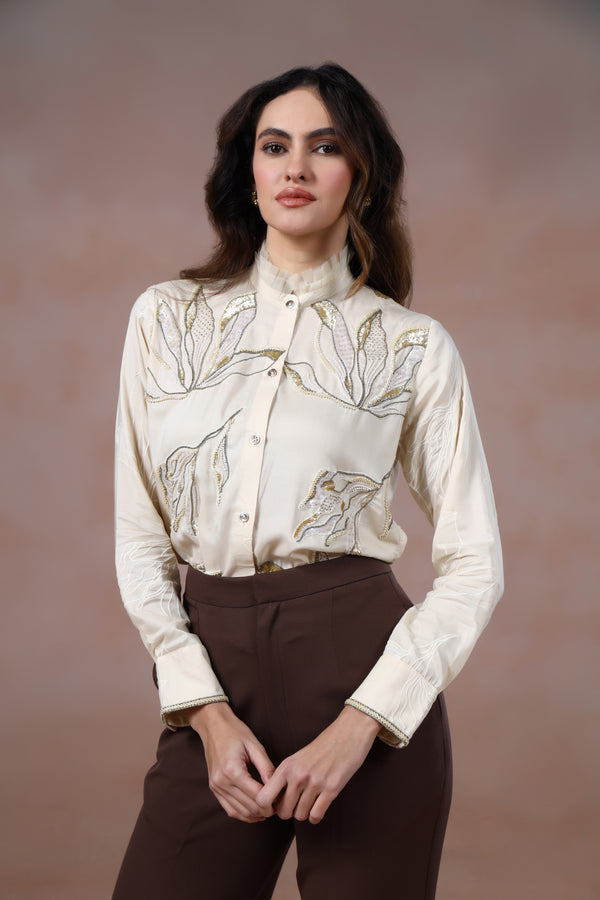Woman wearing a cream floral blouse and brown pants against a brown background