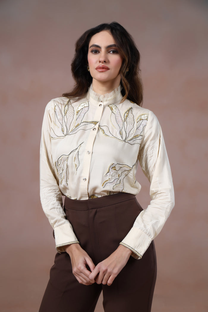 Woman wearing a cream floral blouse and brown pants against a brown background