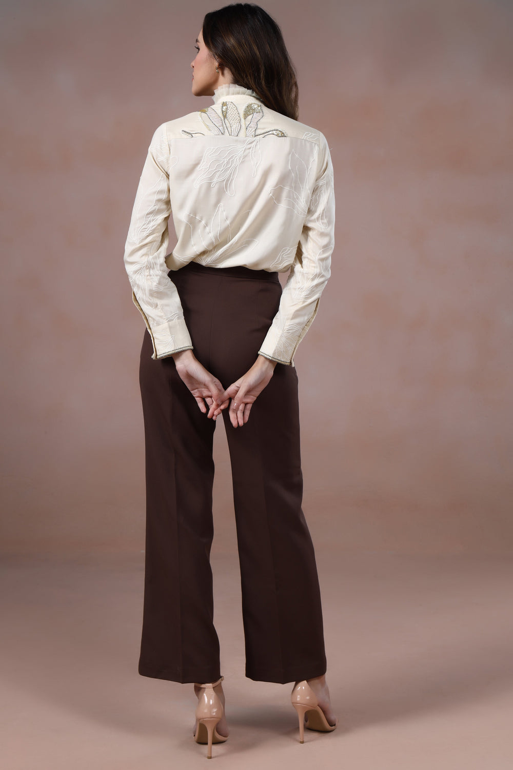 Woman wearing a white blouse and brown pants against a beige background