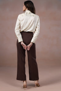 Woman wearing a white blouse and brown pants against a beige background