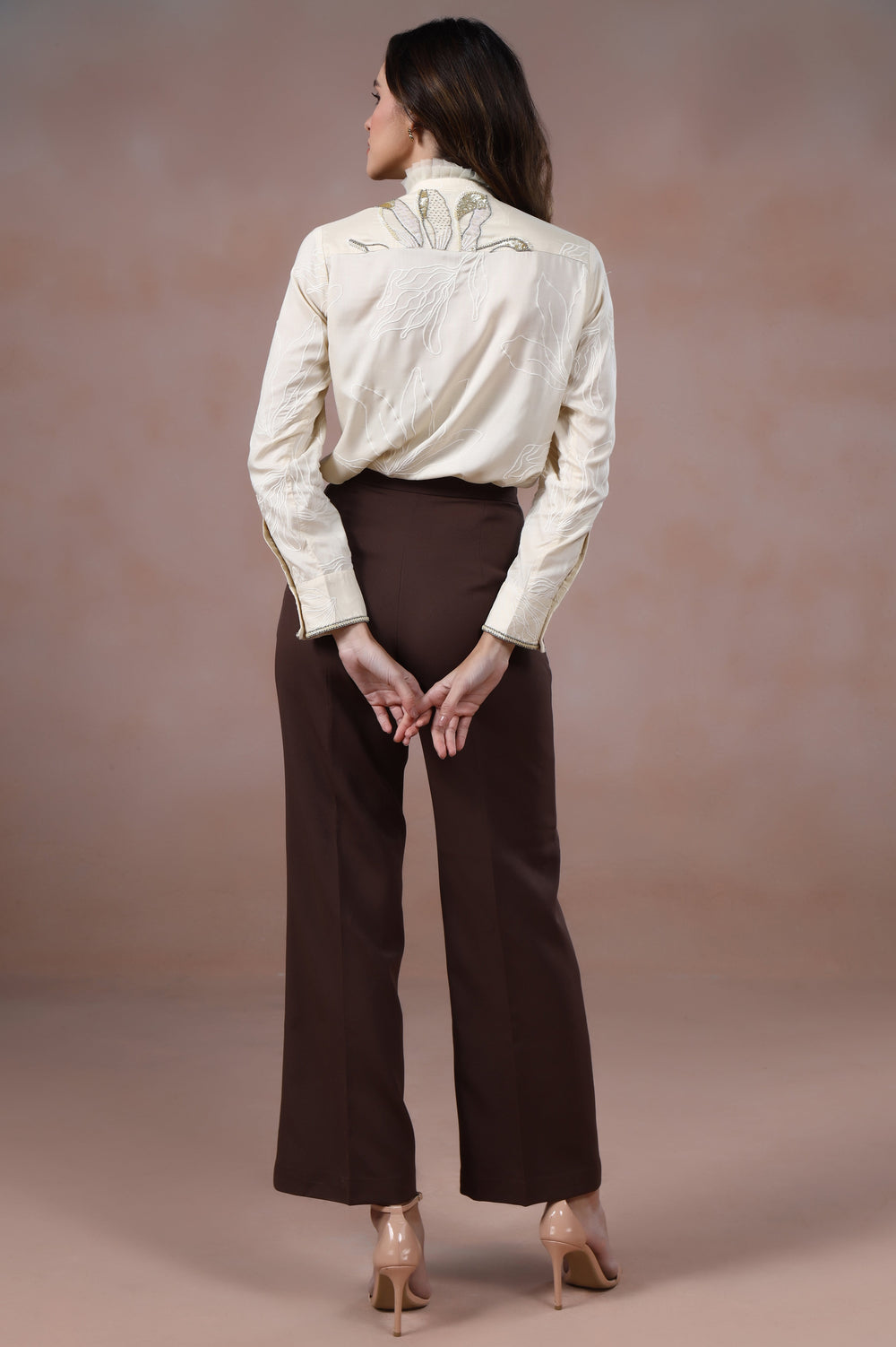 Woman wearing a white blouse and brown pants against a beige background
