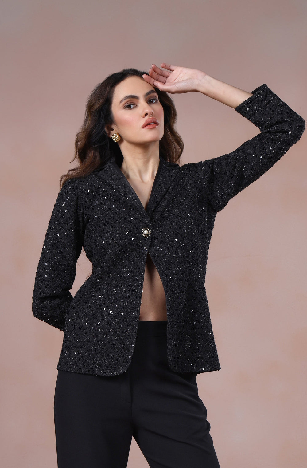 Woman wearing a black suit with flared pants against a beige background