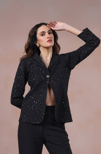 Woman wearing a black suit with flared pants against a beige background