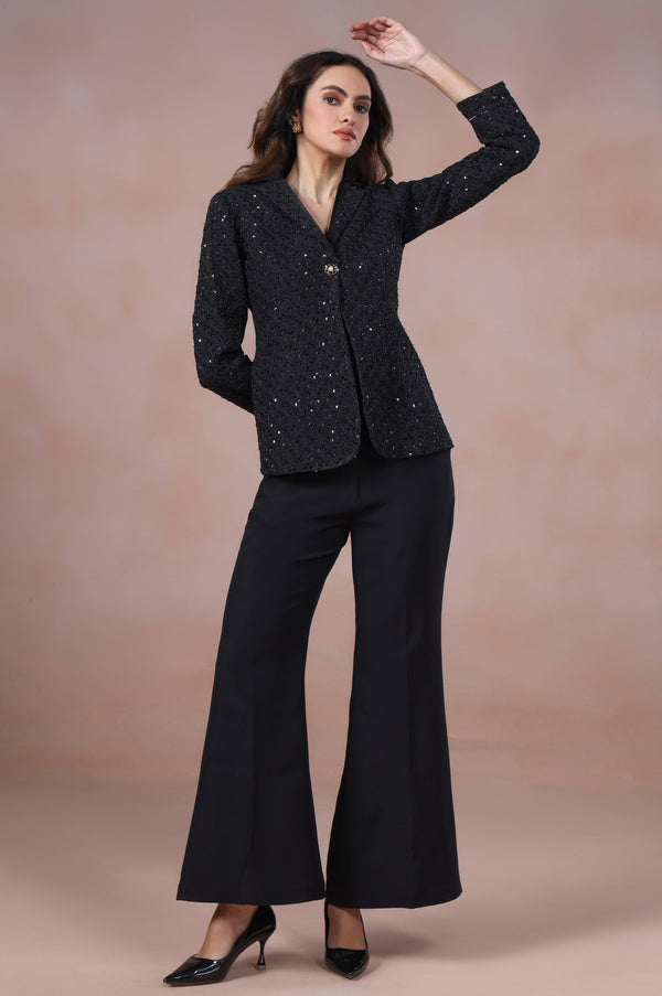 Woman wearing a black suit with a textured pattern against a beige background