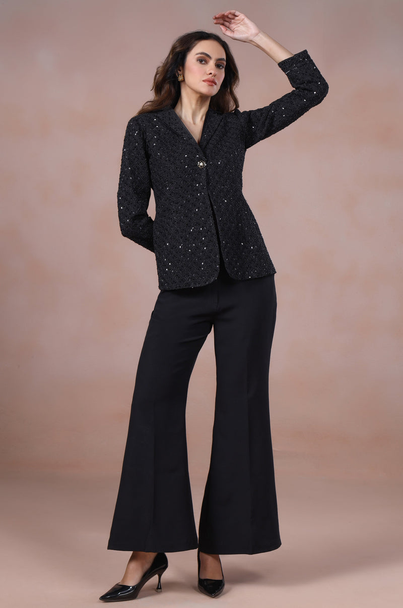 Woman wearing a black suit with a textured pattern against a beige background