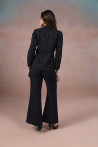 Woman wearing a black sequin top and flared pants against a beige background