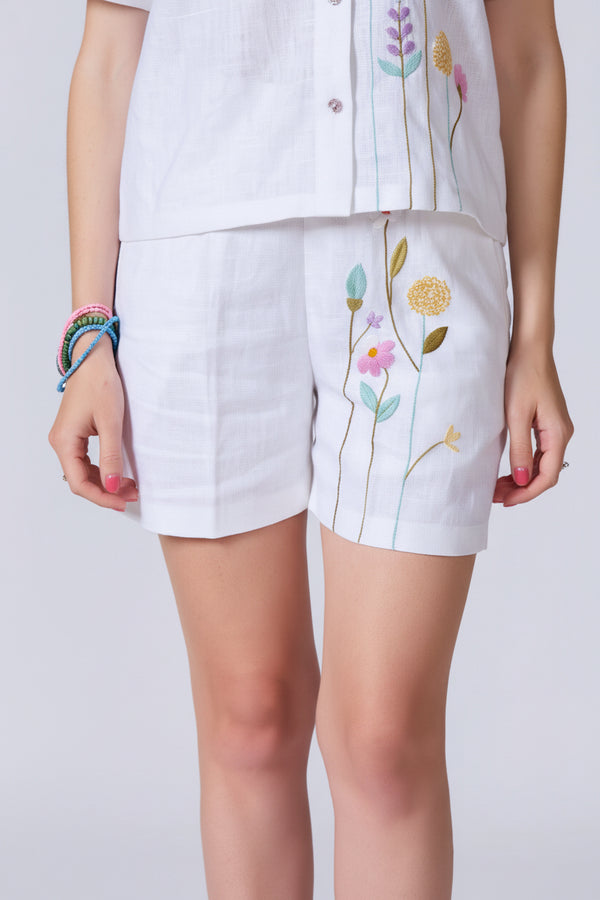 Woman wearing a white outfit with floral embroidery on a plain background